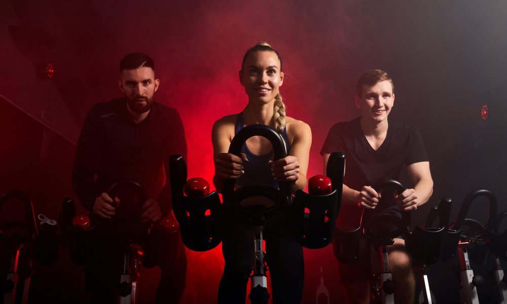 fit people riding exercise bikes in gym, enjoying workout time, in smoky red neon space